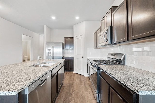 kitchen with sink, appliances with stainless steel finishes, a kitchen island with sink, light hardwood / wood-style floors, and backsplash