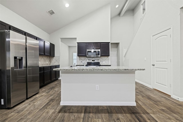 kitchen with an island with sink, dark hardwood / wood-style flooring, decorative backsplash, light stone counters, and stainless steel appliances