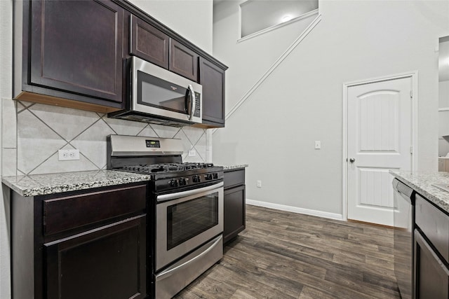 kitchen featuring stainless steel appliances, dark brown cabinets, dark hardwood / wood-style floors, and light stone counters