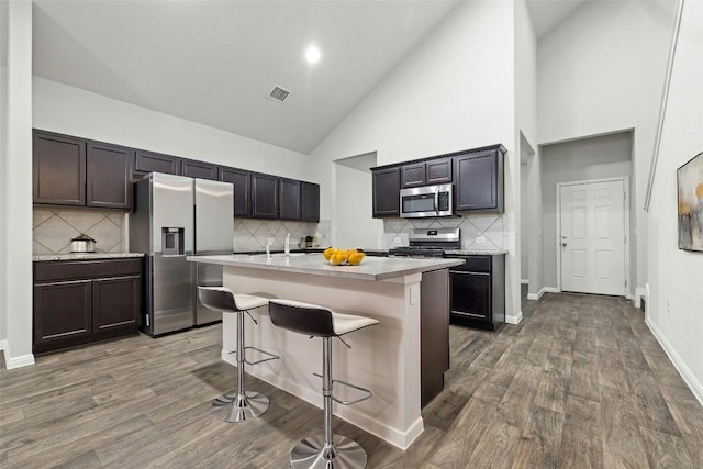 kitchen featuring dark hardwood / wood-style flooring, appliances with stainless steel finishes, a kitchen island with sink, and a kitchen breakfast bar