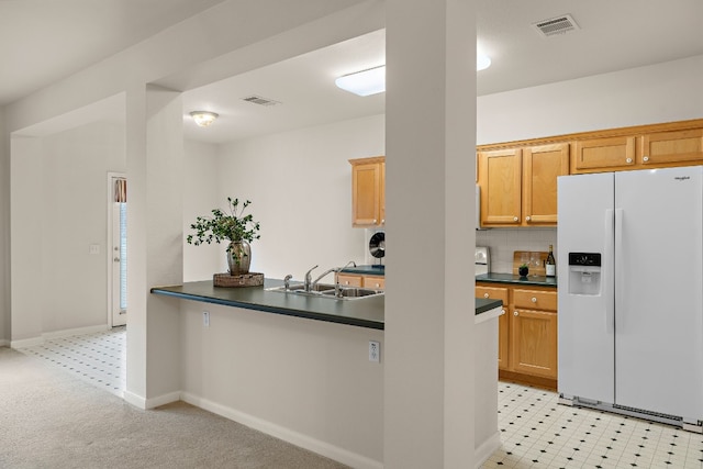 kitchen with dark countertops, visible vents, white fridge with ice dispenser, and a sink