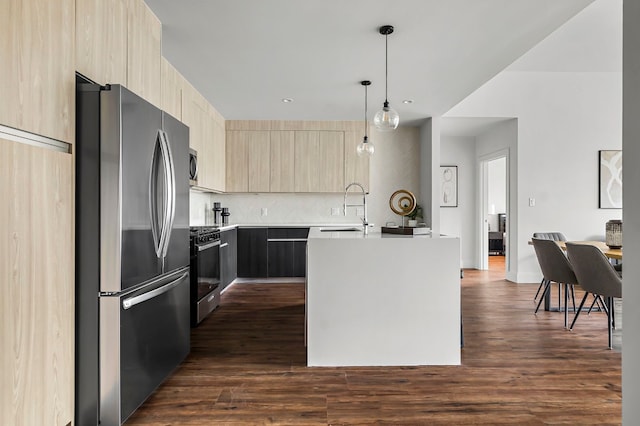 kitchen with light brown cabinetry, sink, decorative light fixtures, appliances with stainless steel finishes, and a kitchen island with sink