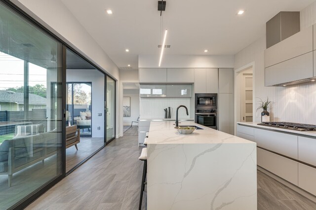 kitchen with sink, light stone counters, appliances with stainless steel finishes, an island with sink, and backsplash