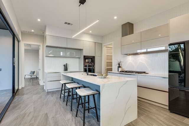 kitchen featuring pendant lighting, a kitchen island with sink, a kitchen bar, built in microwave, and stainless steel gas stovetop