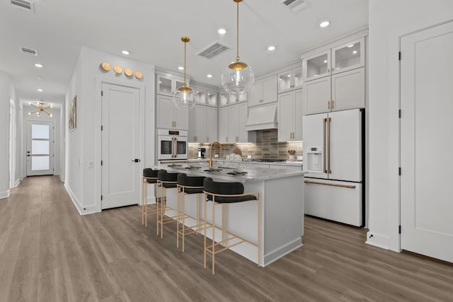 kitchen featuring pendant lighting, white appliances, white cabinetry, an island with sink, and custom exhaust hood