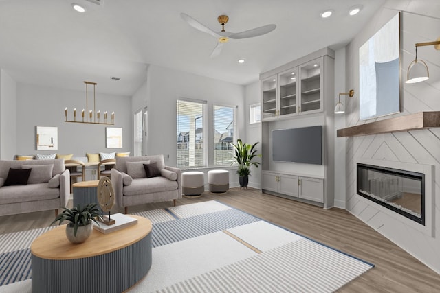 living room with ceiling fan with notable chandelier, a large fireplace, and hardwood / wood-style floors