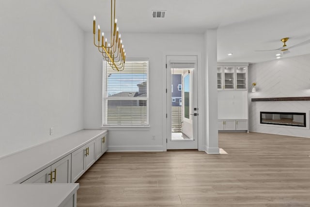 doorway to outside with a large fireplace, ceiling fan with notable chandelier, and light wood-type flooring