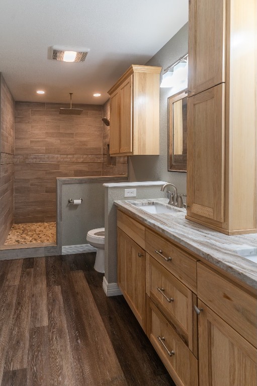 bathroom featuring vanity, hardwood / wood-style floors, toilet, and tiled shower