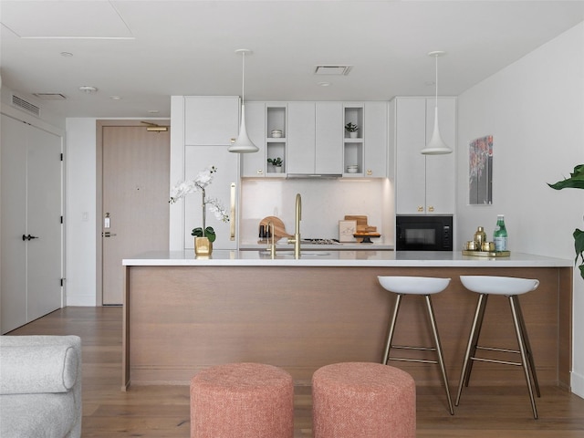 kitchen featuring a kitchen bar, decorative light fixtures, black microwave, and white cabinets