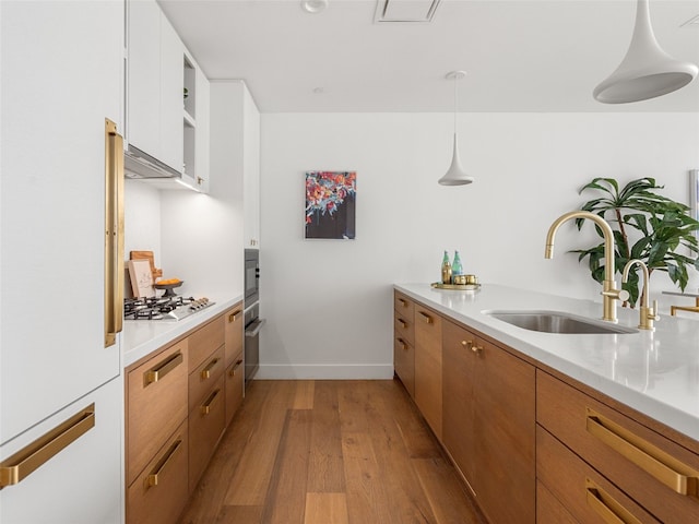 kitchen with stainless steel gas cooktop, sink, white cabinetry, pendant lighting, and light hardwood / wood-style floors