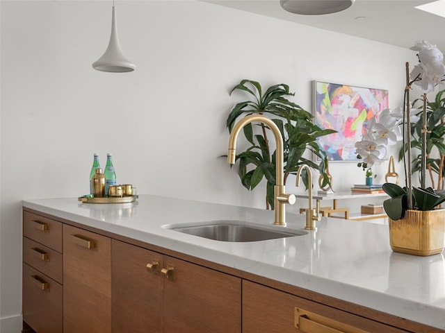 kitchen featuring light stone counters, sink, and hanging light fixtures