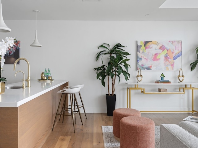 bar featuring sink, hanging light fixtures, and light hardwood / wood-style flooring