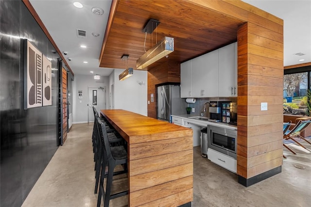 kitchen featuring stainless steel appliances, white cabinets, a sink, wood counters, and concrete floors