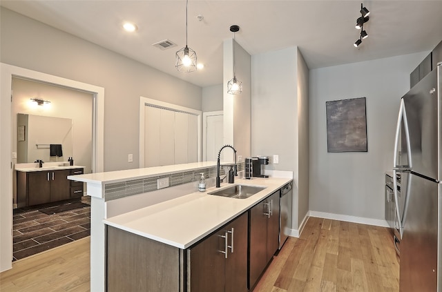 kitchen featuring dark brown cabinetry, light wood finished floors, appliances with stainless steel finishes, light countertops, and a sink