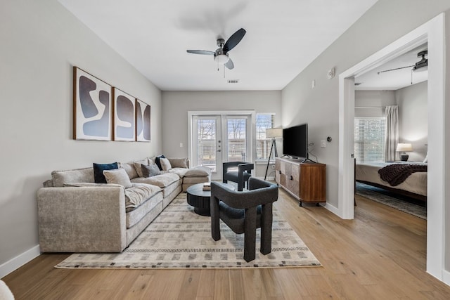 living area featuring baseboards, light wood-style floors, a healthy amount of sunlight, and a ceiling fan