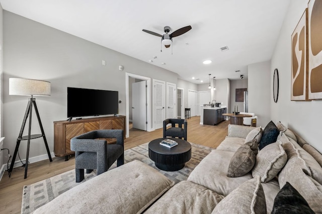 living area with baseboards, a ceiling fan, visible vents, and light wood-type flooring