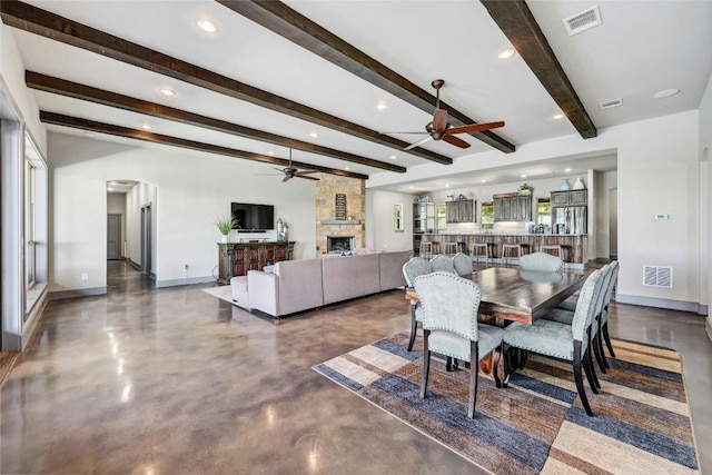 dining area featuring a fireplace, beamed ceiling, and ceiling fan