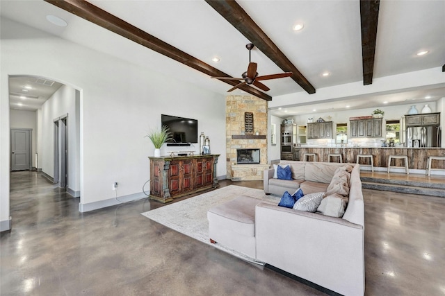 living room featuring ceiling fan, a stone fireplace, and beam ceiling