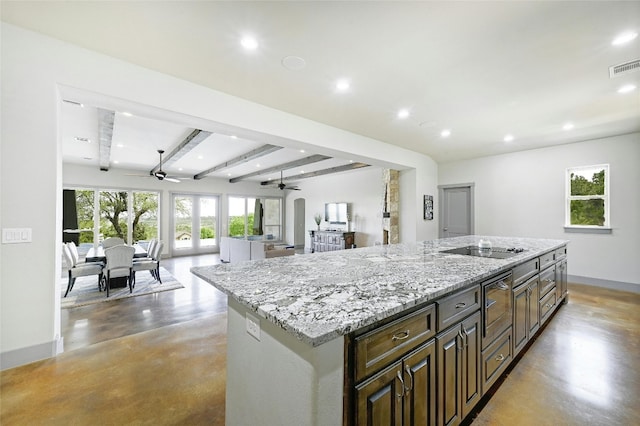 kitchen with concrete flooring, a center island, black electric stovetop, beam ceiling, and light stone countertops