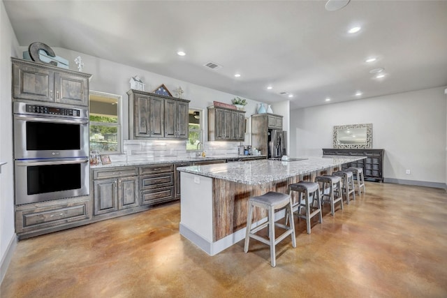 kitchen with a kitchen island, a breakfast bar, decorative backsplash, stainless steel appliances, and light stone countertops