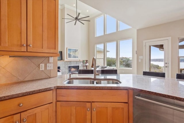 kitchen with sink, stainless steel dishwasher, a tile fireplace, ceiling fan, and decorative backsplash