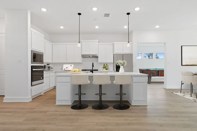 118 Bateleurfrey Cv, Cedar Creek, TX 78612 - kitchen with stainless steel appliances, light wood-style flooring, an island with sink, a kitchen breakfast bar, and white cabinets