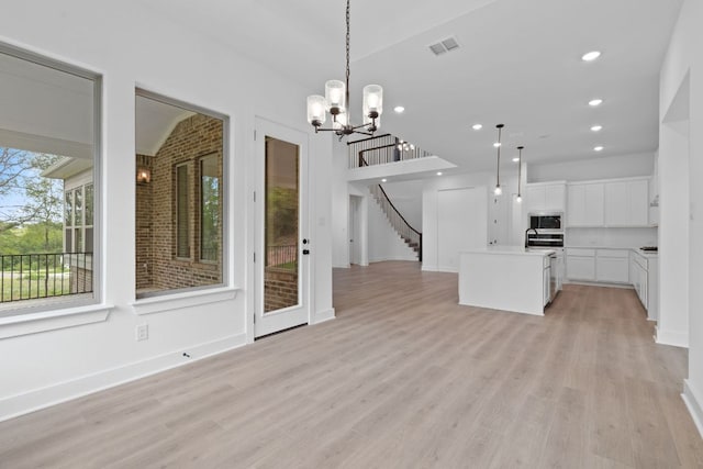 118 Bateleurfrey Cv, Cedar Creek, TX 78612 - kitchen featuring stainless steel microwave, a chandelier, open floor plan, light wood-type flooring, and a kitchen island with sink