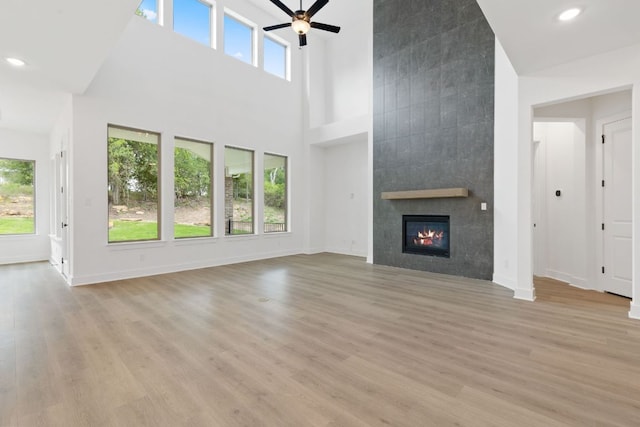 118 Bateleurfrey Cv, Cedar Creek, TX 78612 - unfurnished living room with a towering ceiling, a ceiling fan, a tile fireplace, light wood finished floors, and recessed lighting