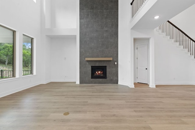 118 Bateleurfrey Cv, Cedar Creek, TX 78612 - unfurnished living room with a towering ceiling, a tile fireplace, light wood-style flooring, and stairs