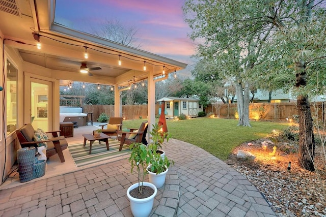 patio terrace at dusk with an outdoor structure, a hot tub, and a lawn