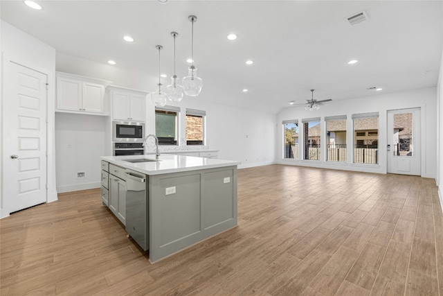 kitchen with appliances with stainless steel finishes, a wealth of natural light, an island with sink, white cabinets, and hanging light fixtures