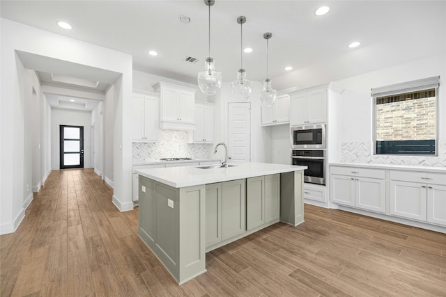 kitchen featuring built in microwave, white cabinetry, a kitchen island with sink, and stainless steel oven