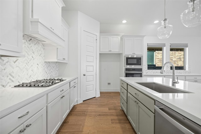 kitchen with white cabinetry, wood-type flooring, sink, hanging light fixtures, and stainless steel appliances