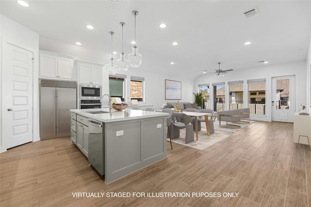 kitchen featuring white cabinetry, built in appliances, decorative light fixtures, light wood-type flooring, and a kitchen island with sink