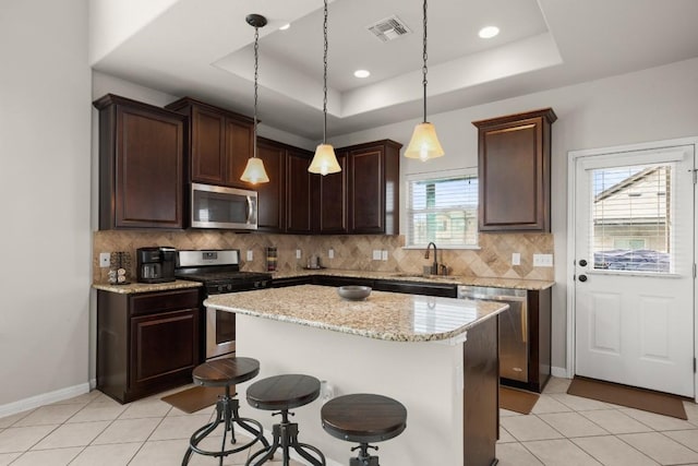 kitchen with a raised ceiling, appliances with stainless steel finishes, a center island, and sink