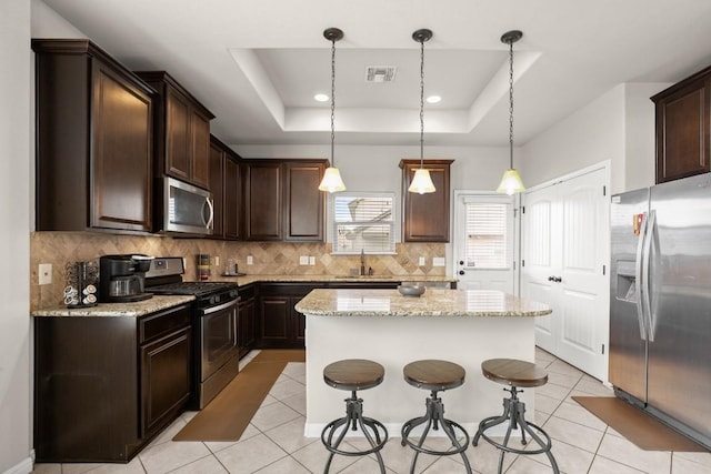 kitchen featuring a center island, appliances with stainless steel finishes, decorative light fixtures, and a raised ceiling