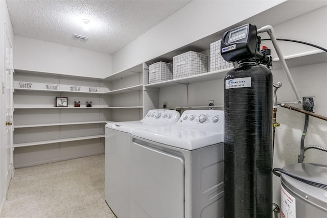 laundry room with water heater, washing machine and dryer, and a textured ceiling