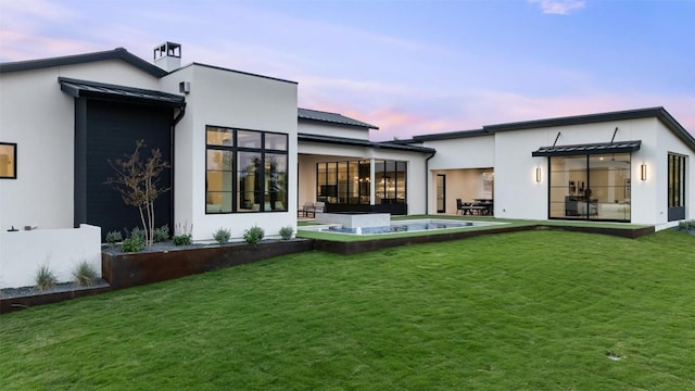 back house at dusk featuring a lawn and a patio area