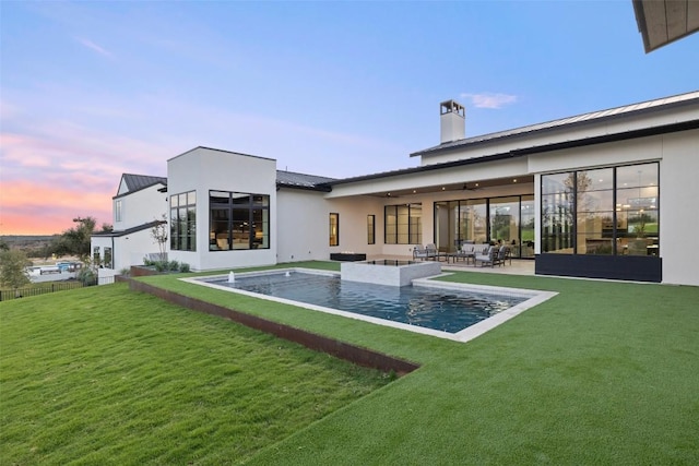 back house at dusk with a patio area and a lawn