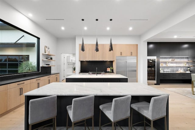 kitchen with pendant lighting, a breakfast bar area, a spacious island, light stone counters, and built in fridge