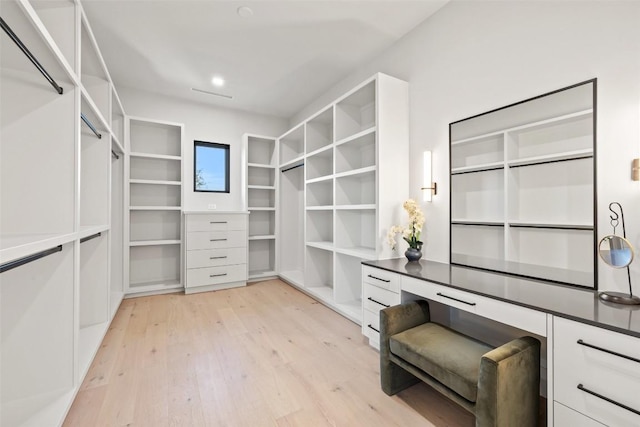 spacious closet with built in desk and light hardwood / wood-style floors