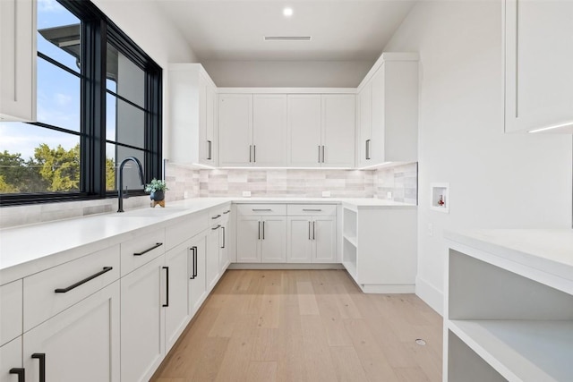 kitchen featuring sink, white cabinets, backsplash, and light hardwood / wood-style flooring