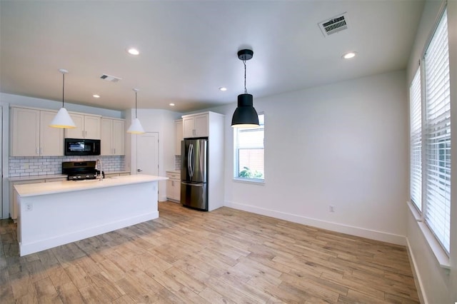 kitchen with pendant lighting, light hardwood / wood-style flooring, backsplash, stainless steel appliances, and a center island with sink