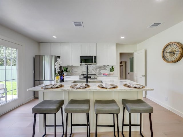 kitchen with light stone countertops, appliances with stainless steel finishes, a kitchen island with sink, and white cabinets