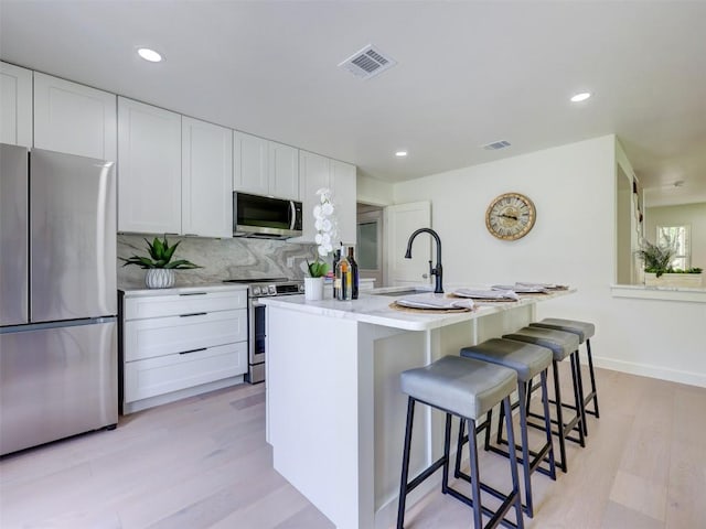 kitchen featuring a breakfast bar area, stainless steel appliances, white cabinets, and a center island with sink