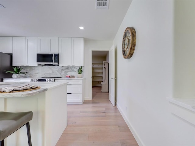 kitchen with a breakfast bar, tasteful backsplash, light stone counters, light hardwood / wood-style floors, and white cabinets