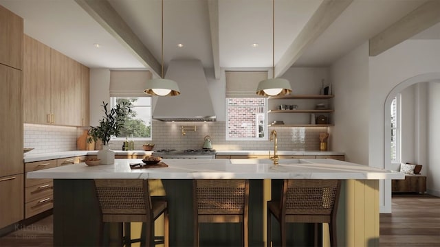 kitchen with a kitchen breakfast bar, beam ceiling, a center island with sink, and wall chimney range hood