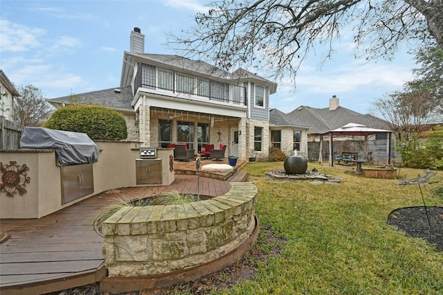 back of property with an outdoor kitchen, a gazebo, a balcony, a lawn, and a wooden deck