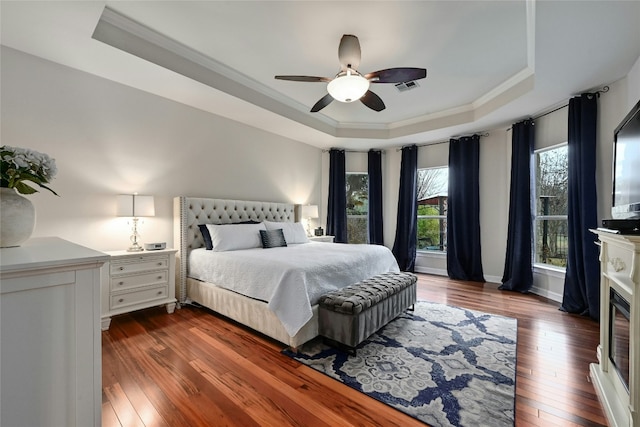 bedroom featuring crown molding, dark hardwood / wood-style floors, ceiling fan, and a tray ceiling