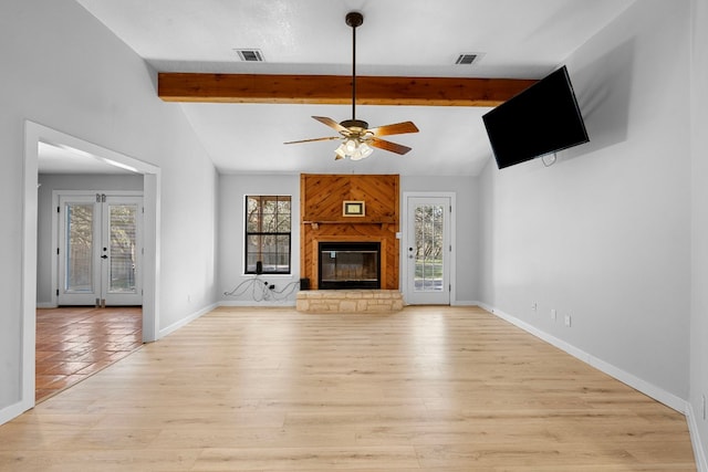 unfurnished living room featuring ceiling fan, a fireplace, lofted ceiling with beams, french doors, and light wood-type flooring